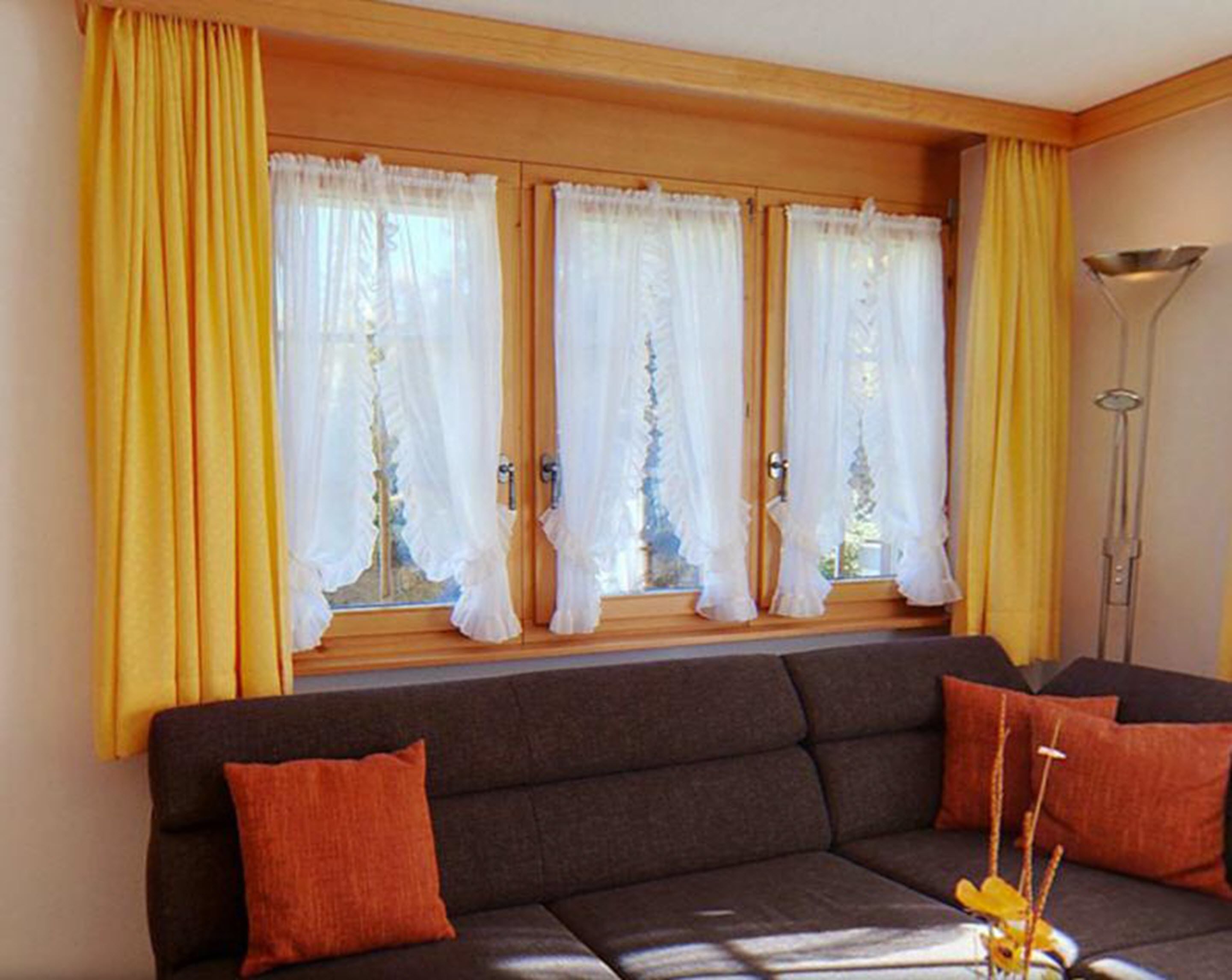 Ein Wohnzimmer mit einem dunklen Sofa, gelben Vorhängen und einer Stehlampe.