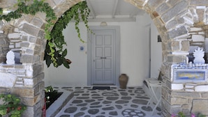 A stone archway leading to a door, with a tiled floor and a small white chair to the right. - Heliolithos Blue Bay (Paros)