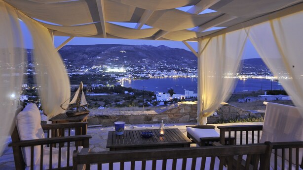 An outdoor dining area with a view of a coastal town at dusk. - Heliolithos Blue Bay (Paros)