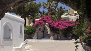 A street scene with a white building, a stone archway, and pink bougainvillea flowers. - Heliolithos Blue Bay (Paros)