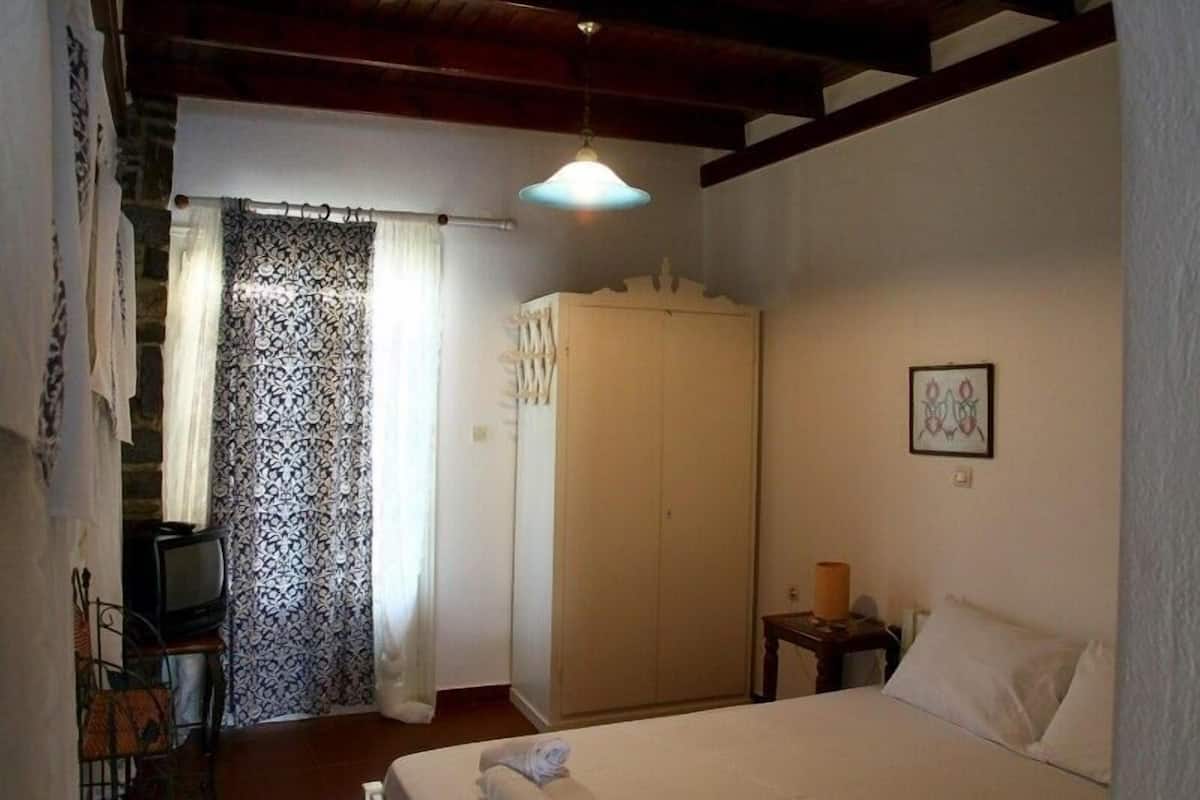 A bedroom with a bed, a wardrobe, a television, and a framed picture on the wall.