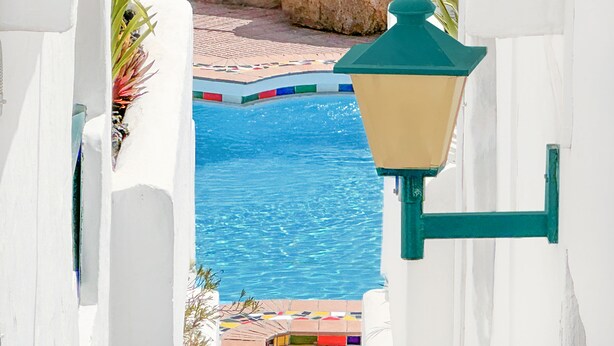 Ett poolområde med en kakelbeklädd terrass, en lyktstolpe och en stenmur.