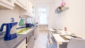 A modern kitchen with white cabinets, a blue kettle, and a dining area with a table set for two. - Zimmervermietung Härtig (Berlin)