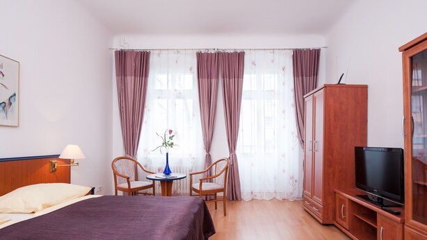 A hotel room with a bed, a TV, a wooden cabinet, a chair, a small table, and a vase with flowers. - Zimmervermietung Härtig (Berlin)