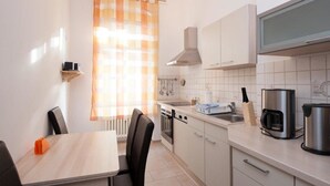 A compact kitchen with a dining area, featuring a stove, oven, sink, and modern appliances. - Zimmervermietung Härtig (Berlin)