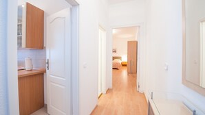 A narrow hallway with a wooden counter and cabinets, leading to a bedroom with a bed and nightstand. - Zimmervermietung Härtig (Berlin)