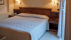 A hotel room with a wooden ceiling, a large bed with a white bedspread, two bedside lamps, and a nightstand with a phone and remote control.