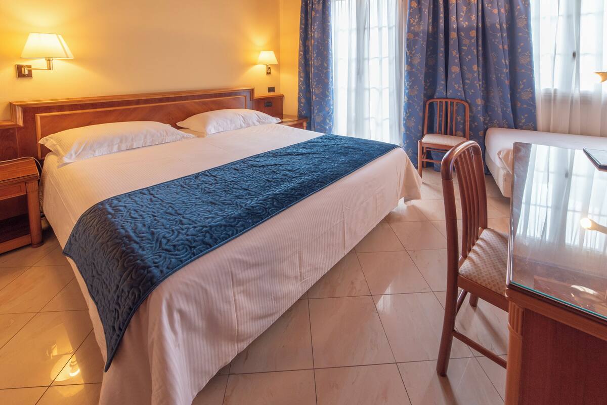 A hotel room with a large bed, two bedside lamps, a wooden nightstand, a chair, and a small table.