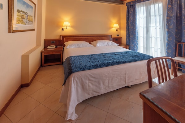 A hotel room with a bed, bedside tables, a desk, and a chair.