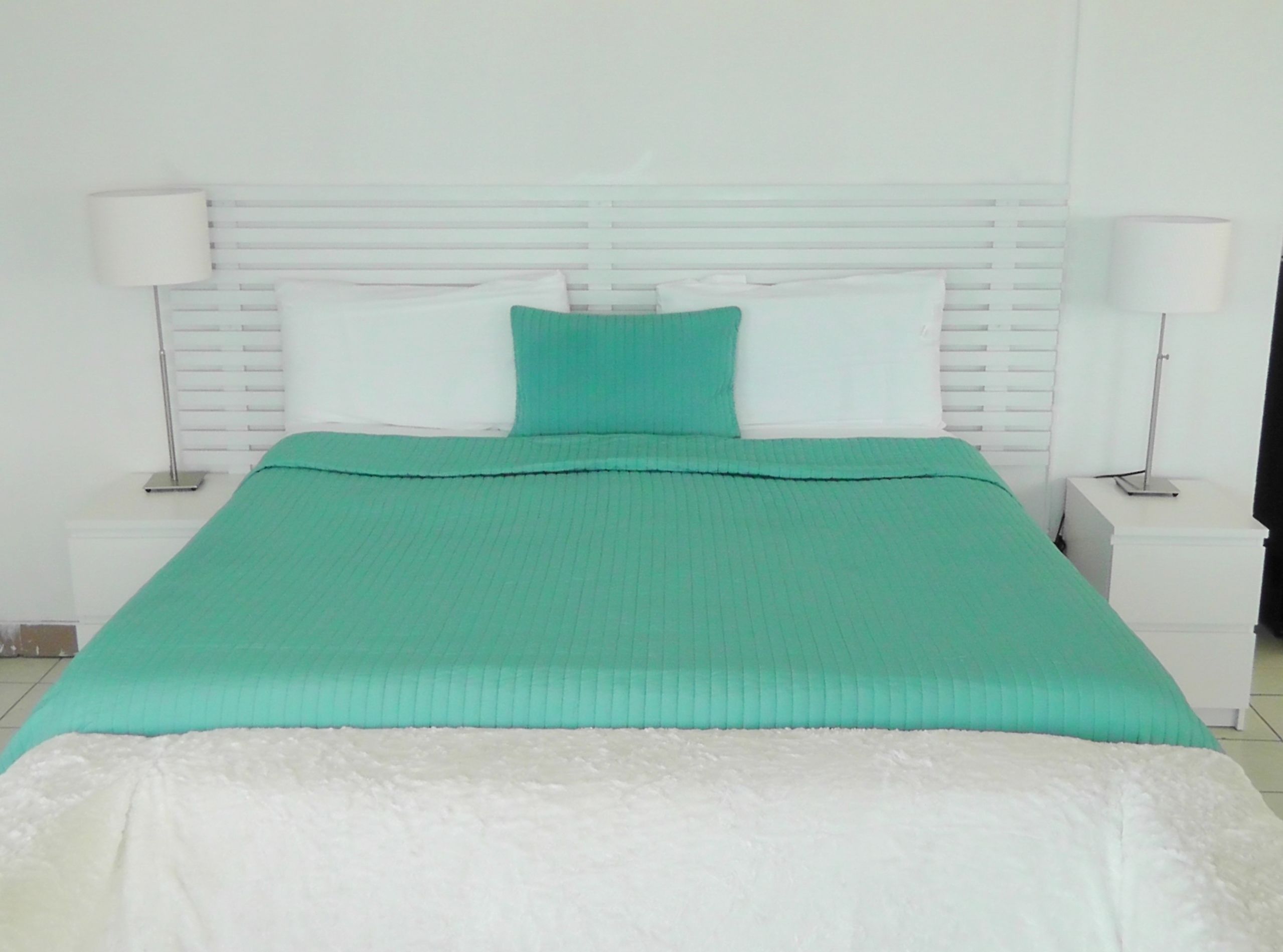 A neatly made bed with a green and white bedspread, white pillows, and a white headboard.