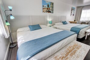 Hotellihuoneessa on kaksi sänkyä, joissa kummassakin on sininen peitto, valkoiset vuodevaatteet ja vaakasuorista laudoista tehty pääty. Huoneessa on myös työpöytä tuolilla, lamppu ja seinällä oleva taulu.