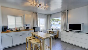 A modern kitchen with white cabinets, a wooden table, and a TV. - Snooze (Fort Lauderdale)
