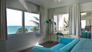 A room with a large window overlooking the ocean, a bed, a desk, and a chair. - Snooze (Fort Lauderdale)