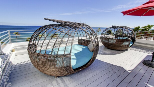 Two wicker swing chairs with blue cushions on a wooden deck overlooking the ocean. - Snooze (Fort Lauderdale)