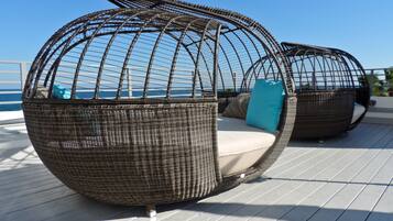 Two spherical wicker chairs with cushions on a deck with a view of the sea.