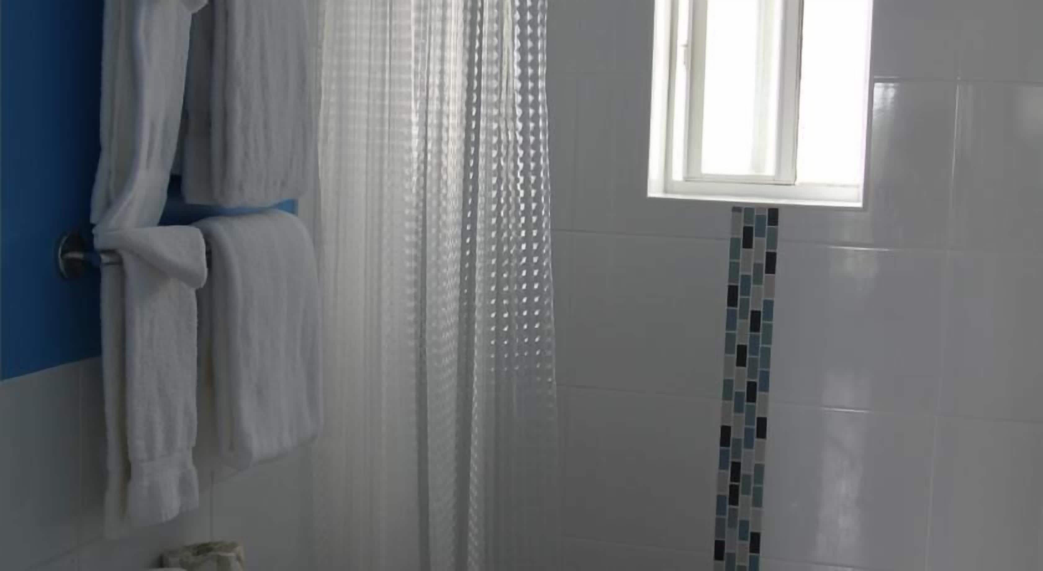 A bathroom with a shower curtain, a window, and a tiled wall.