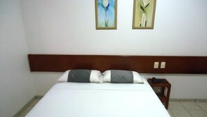 Une chambre d’hôtel avec un lit, une tête de lit en bois, une table de chevet avec un téléphone et deux tableaux encadrés au mur.