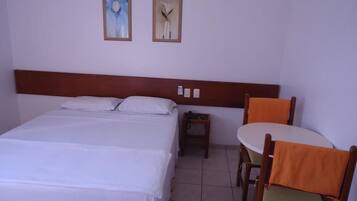 Quarto de hotel com uma cama grande, uma mesa pequena, duas cadeiras e duas imagens emolduradas na parede.