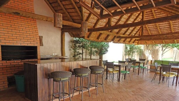 Un espace bar extérieur avec des murs en briques, un plafond en bois et un écran de télévision. On y trouve plusieurs tabourets de bar et des tables avec des chaises.