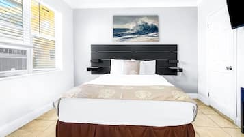 Una camera da letto con un letto, una finestra con persiane, un quadro raffigurante un'onda e una televisione appesa al muro.