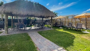 A thatched-roof outdoor seating area with tables and chairs, surrounded by a well-maintained lawn and a brick pathway. - Hollywood Beach Flamingo (Hollywood)