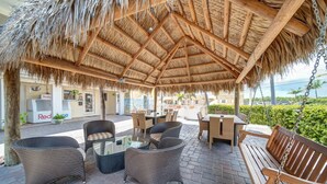 An outdoor patio with wicker furniture, a wooden bench, and a thatched roof. - Hollywood Beach Seagull (Hollywood)