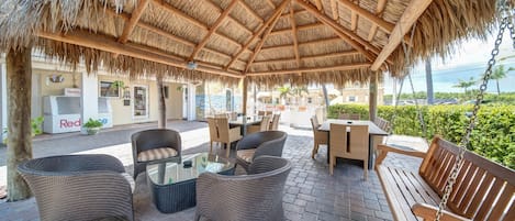 An outdoor patio with wicker furniture, a wooden bench, and a thatched roof.