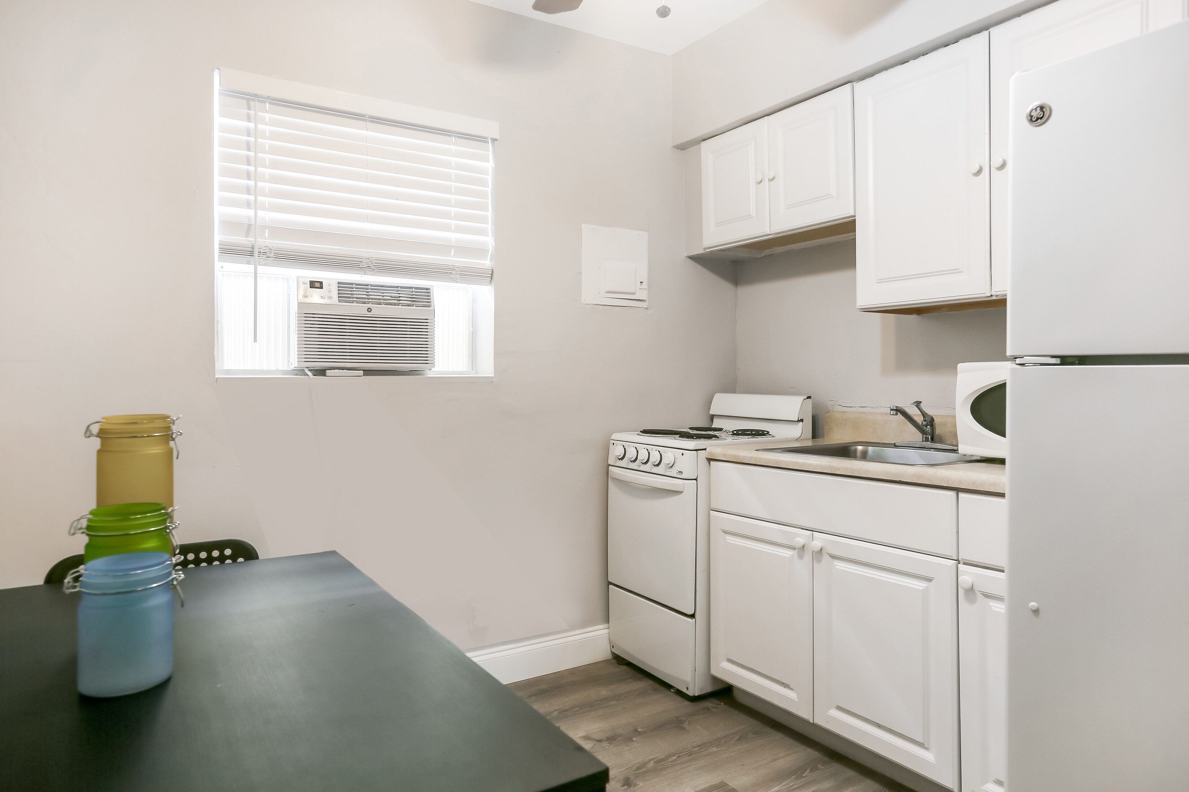 A compact kitchen with white cabinets, a stove, a microwave, and a window with blinds.