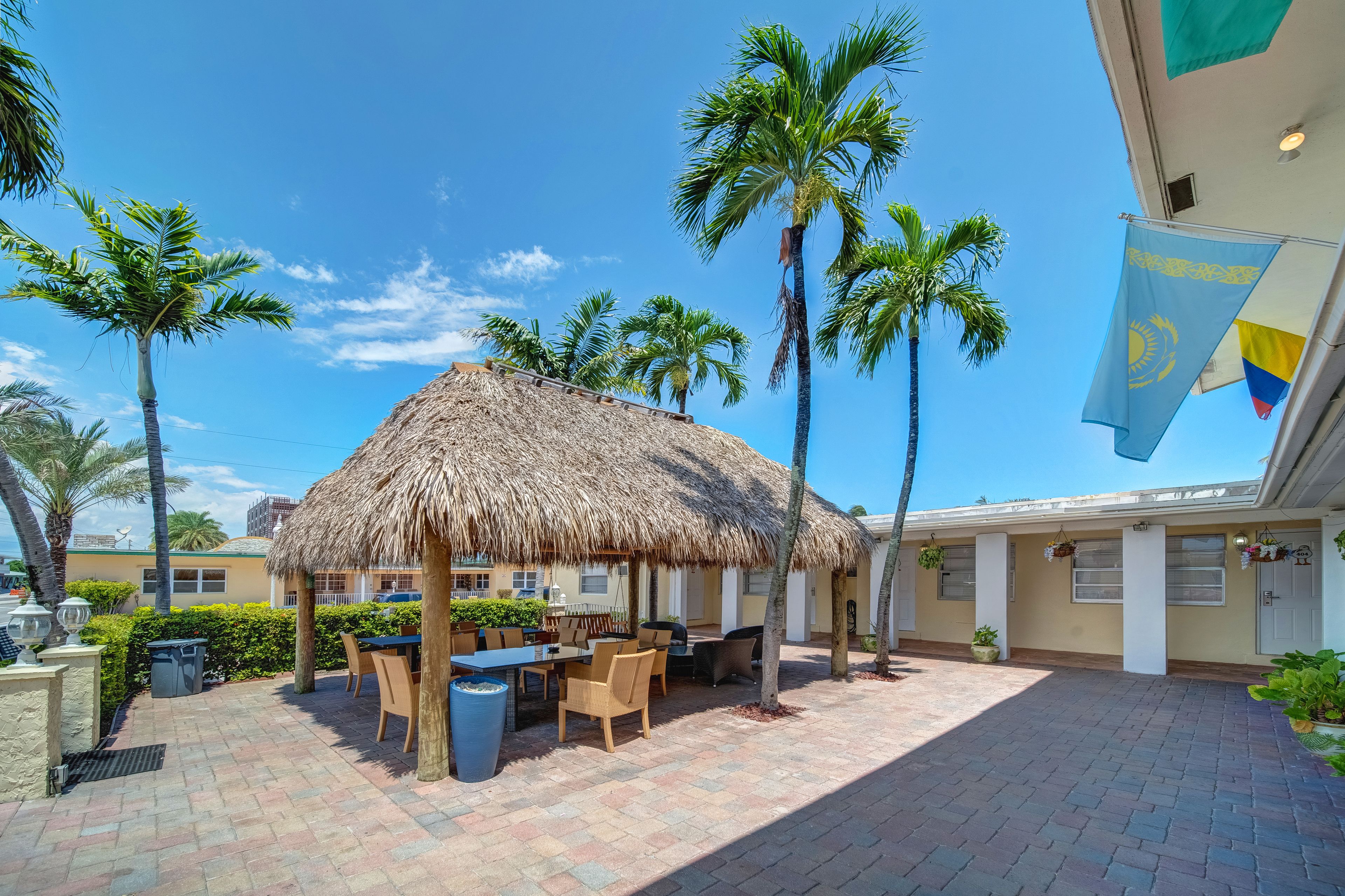 A patio area with a thatched-roof structure, outdoor seating, and palm trees.