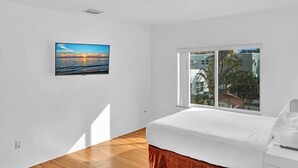 A bedroom with a bed, a window with a view of buildings, and a painting on the wall. - Hollywood Beach Seagull (Hollywood)