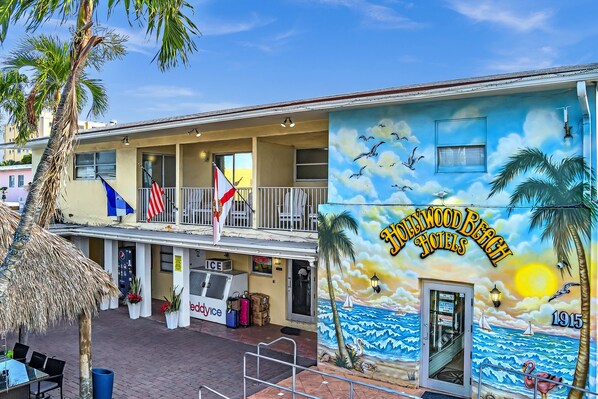 Un edificio de dos pisos con un mural de una escena de playa y el nombre Hollywood Beach Hotels.