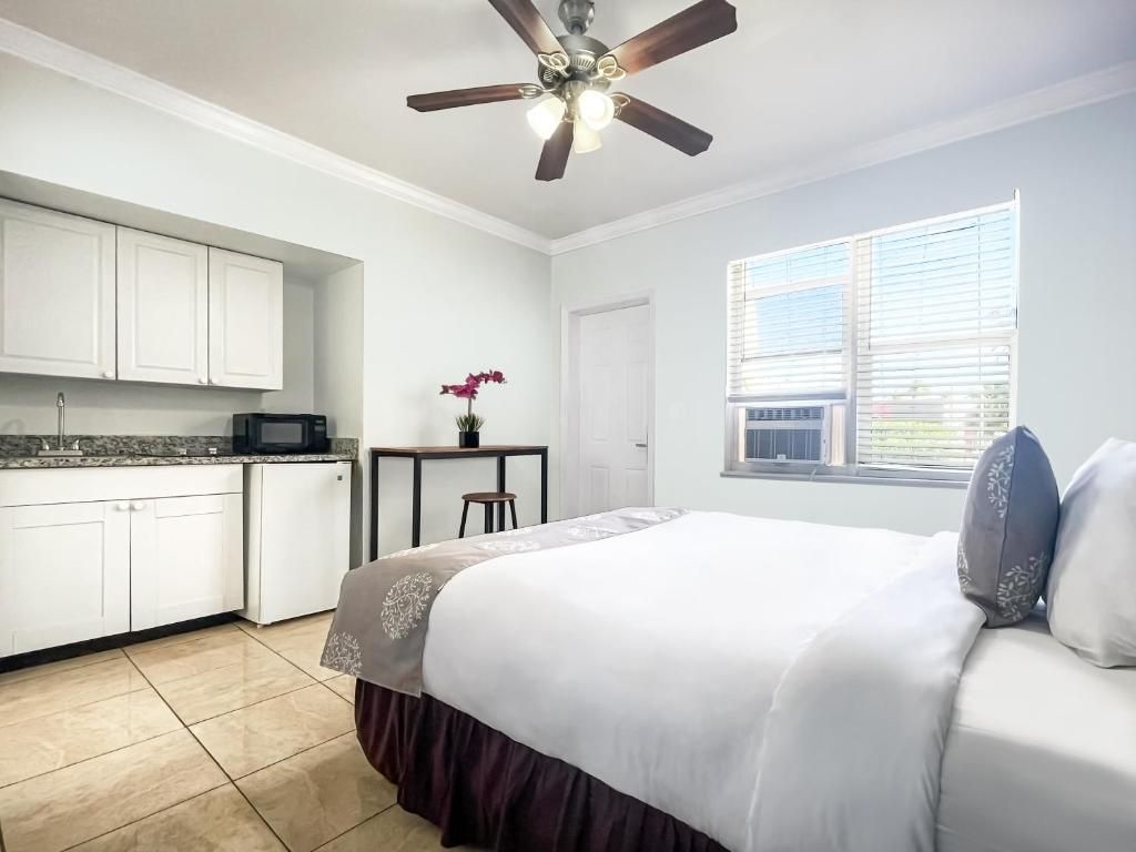 A bedroom with a bed, a desk, a chair, a window with blinds, and a ceiling fan.