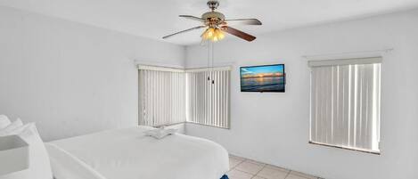 A bedroom with a bed, a ceiling fan, a window with blinds, and a picture on the wall.