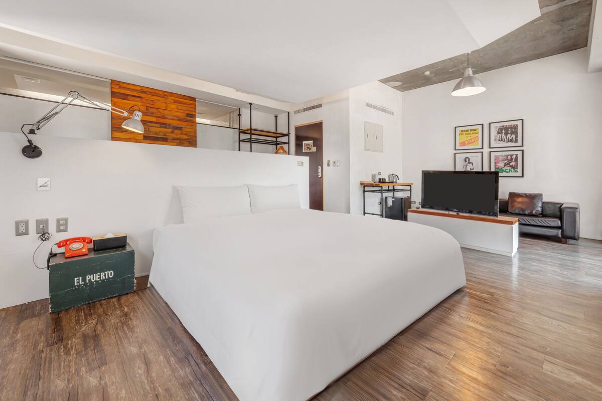 A modern hotel room with a large bed, a desk, a TV, and a wooden accent wall.