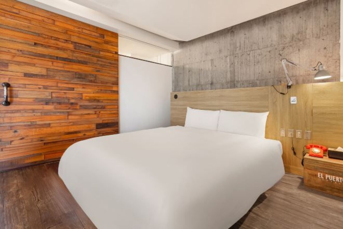Una habitación de hotel moderna con un panel decorativo de madera, una cama grande, un escritorio con teléfono y una mesita de noche con lámpara.