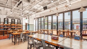 Una biblioteca amplia con mesas y sillas de madera, ventanas grandes y luces en el techo.