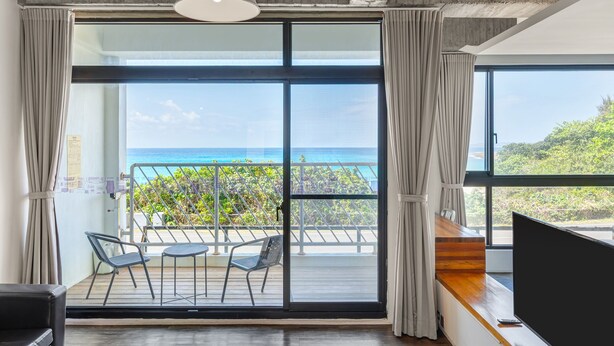 Una habitación moderna con un amplio ventanal corredero que da a un balcón con vistas al océano.