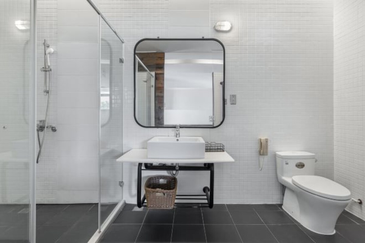 Un baño moderno con cabina de ducha de vidrio, un lavabo blanco sobre encimera negra, un espejo sobre el lavabo y un inodoro blanco.