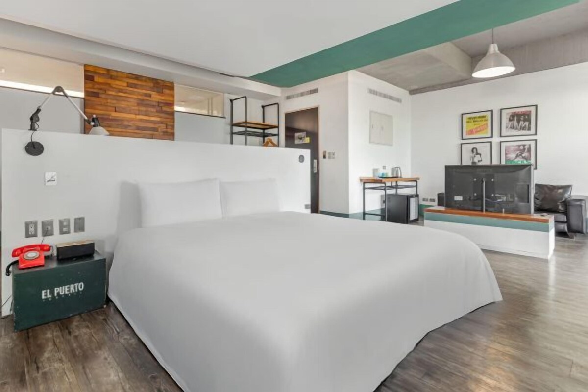 A modern hotel room with a large bed, a desk with a computer, a small seating area, and a wooden accent wall.