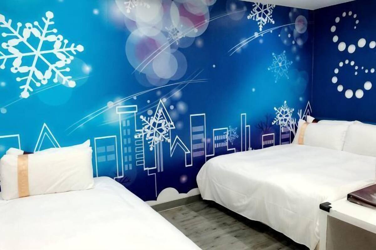 A hotel room with two beds, a cityscape mural on the wall, and a wooden floor.