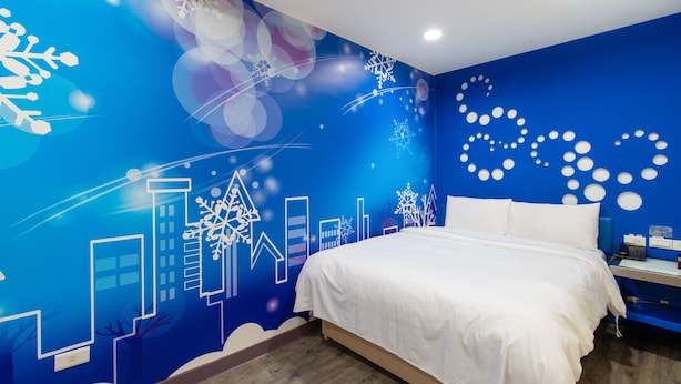 A bedroom with a blue wall featuring a cityscape mural, a white bed, and a nightstand with a lamp. - Giant Rich King Plaza Hotel (Taipei)