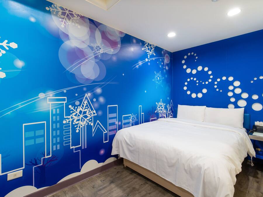 A bedroom with a blue wall featuring a cityscape mural, a white bed, and a nightstand with a lamp.