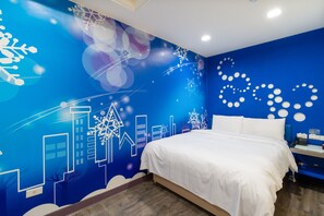 Un dormitorio con pared azul decorada con un mural de paisaje urbano, una cama blanca y una mesita de noche con lámpara.