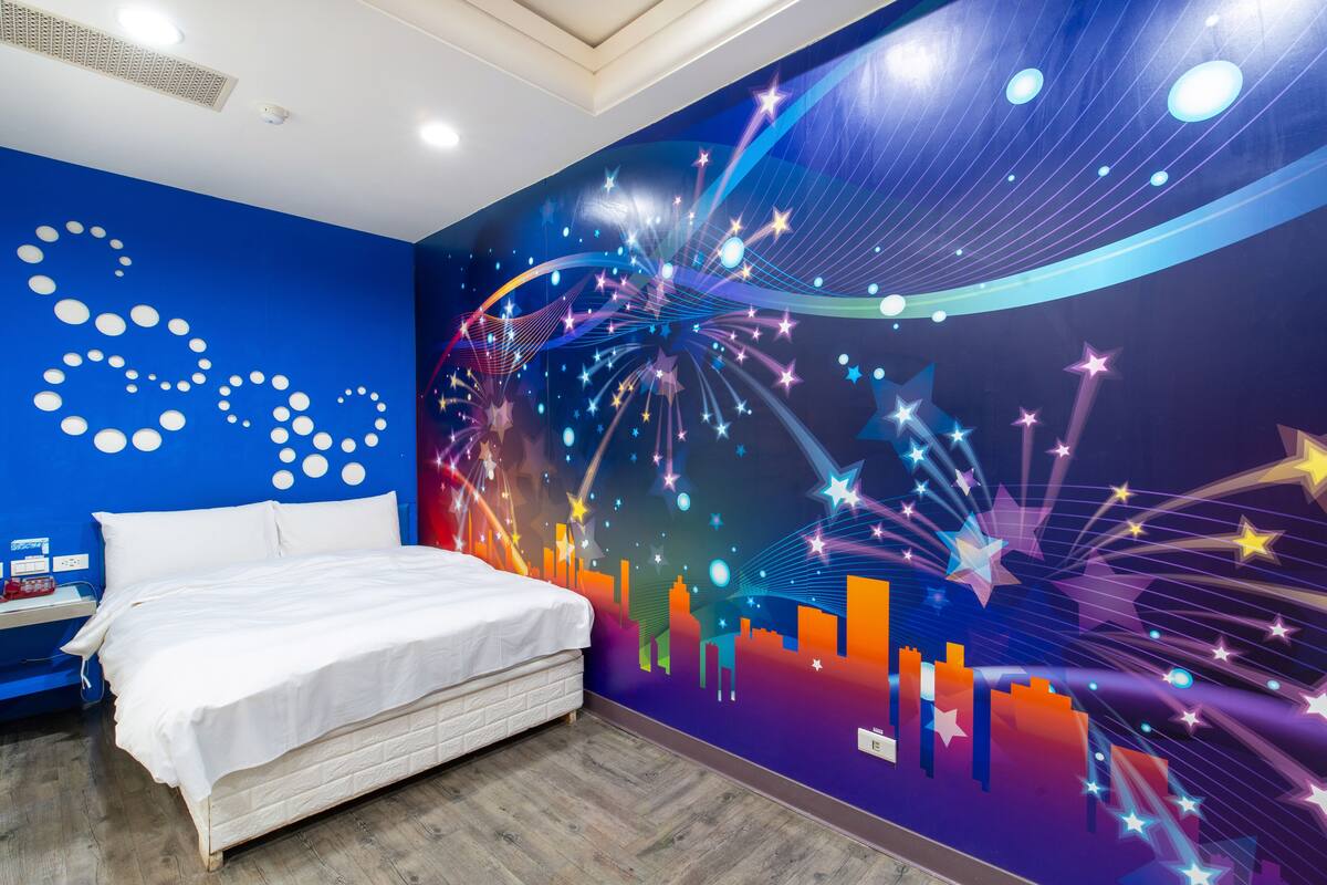 A bedroom with a bed, a nightstand, and a wall mural with abstract designs.