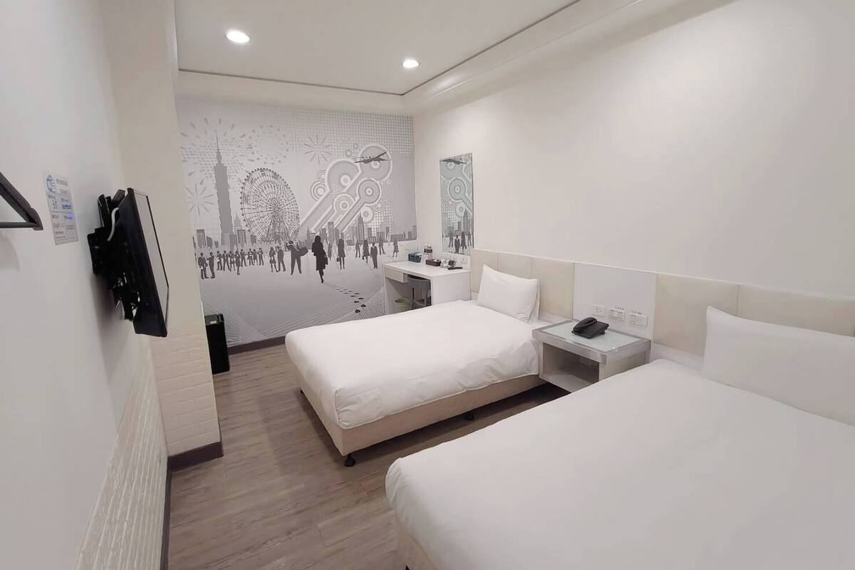A hotel room with two beds, a desk, and a wall mural.