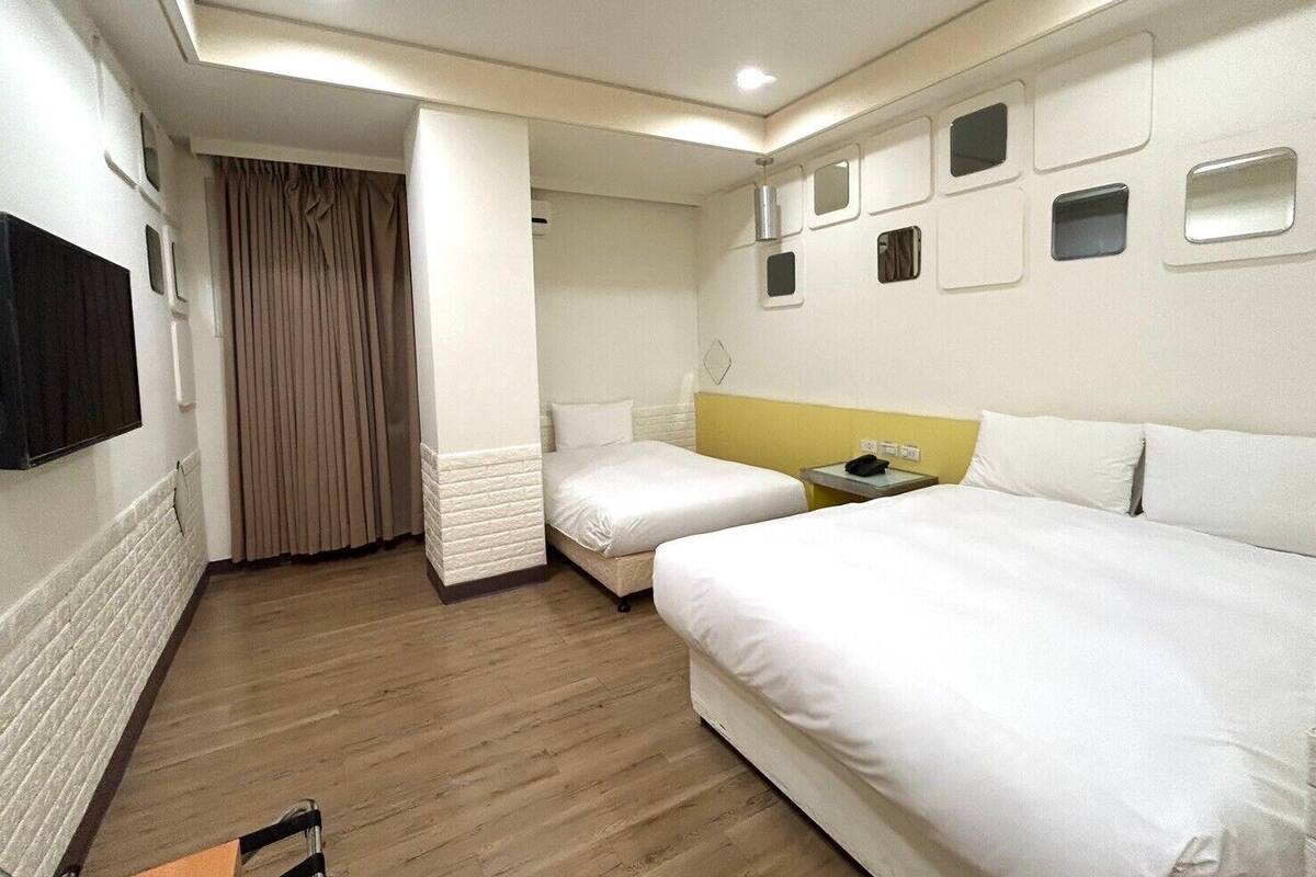 A hotel room with two beds, a small table with a phone, and a TV mounted on the wall.