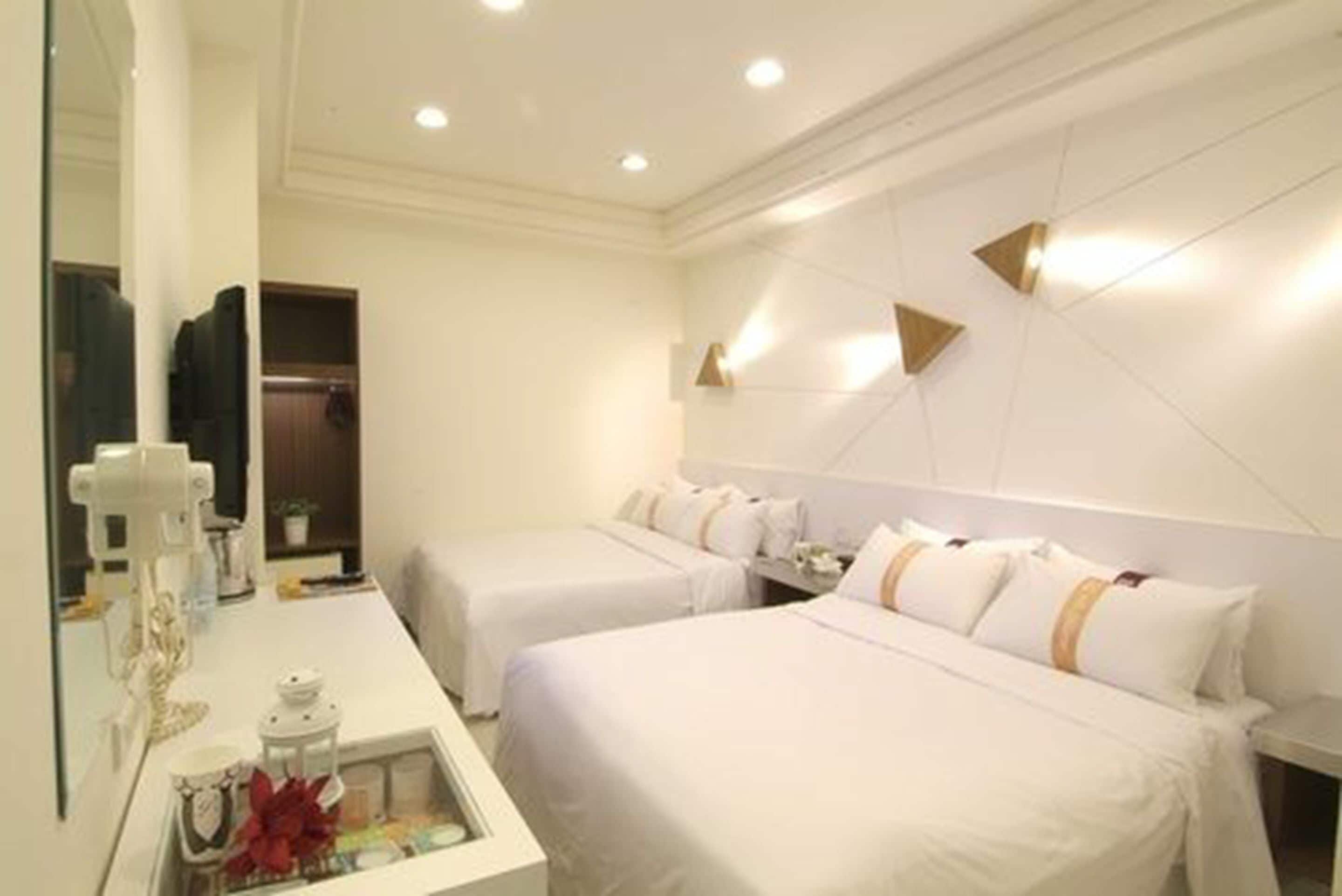 A hotel room with two beds, a bedside table, a mirror, and a wardrobe.