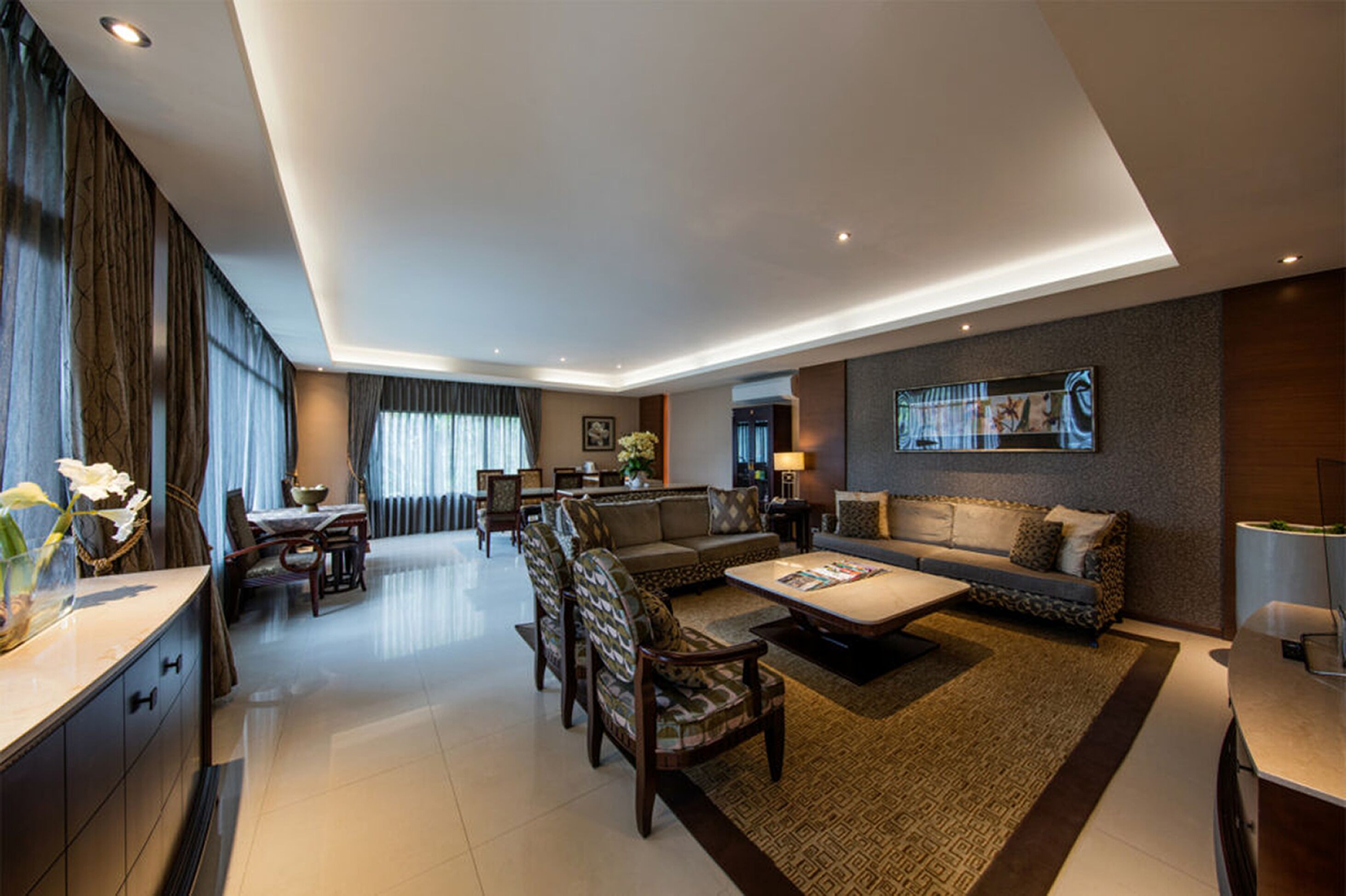 A modern living room with a sofa, coffee table, and chairs. There is a dining area with a table and chairs. The room has a large window with curtains.