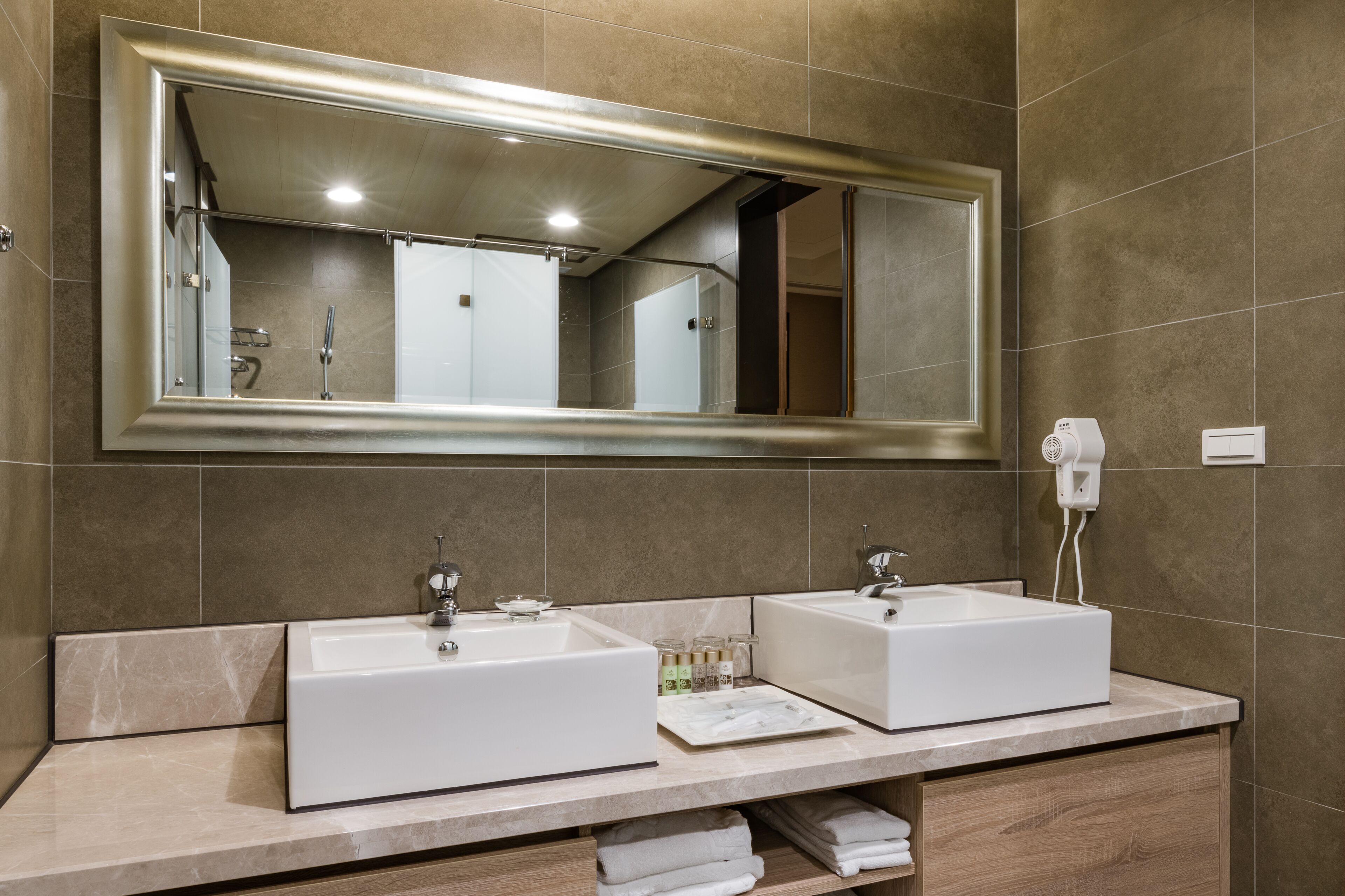 A bathroom with two sinks, a large mirror, and a hairdryer on the wall.