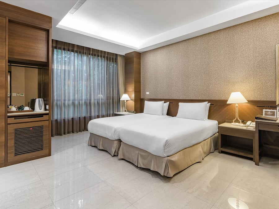 A hotel room with a large bed, a desk with a lamp, a wardrobe, and a mirror.